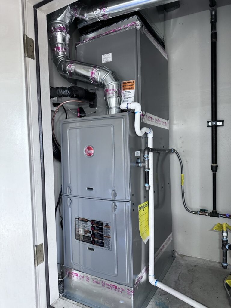 A Rheem gas furnace installed in a closet with metal ductwork, PVC condensate piping, and black gas supply lines.